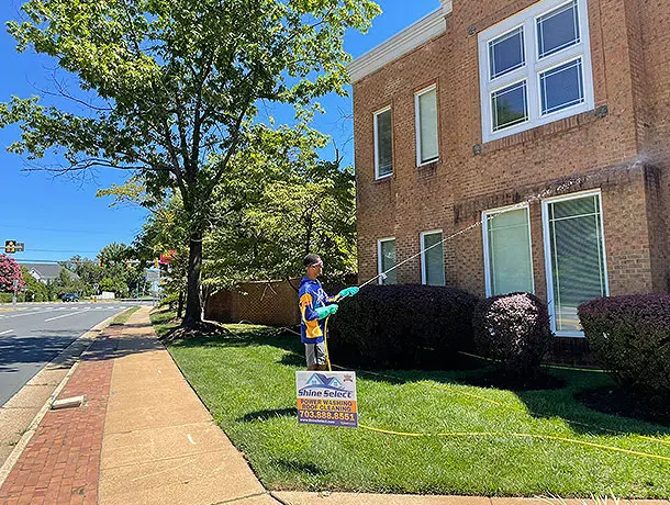 Shine Select employee outside of a two story brick business using power washing equipment to clean.