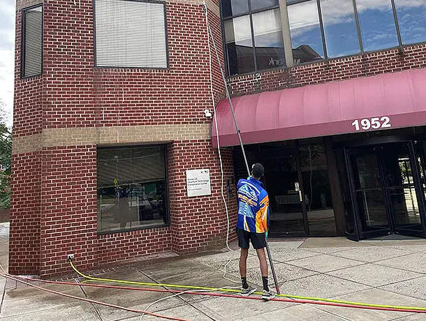 shine select employee using an extension pole to pressure wash a two story building storefront