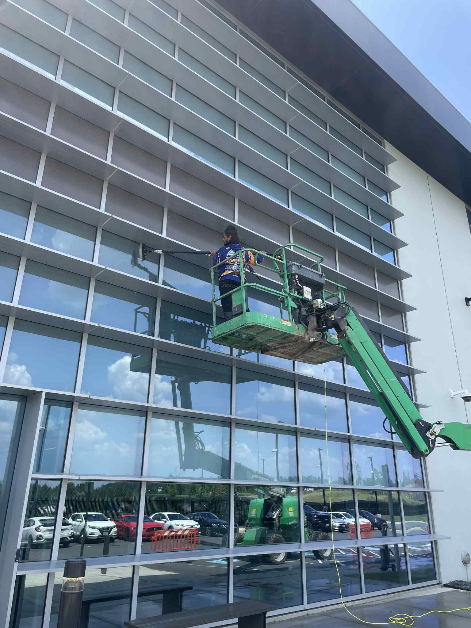 Shine Select employee on a green lift performing pressure washing on a tall building with windows